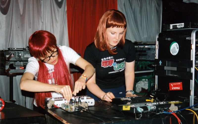 Two women standing at a desk, making adjustments to sound control equipment. 