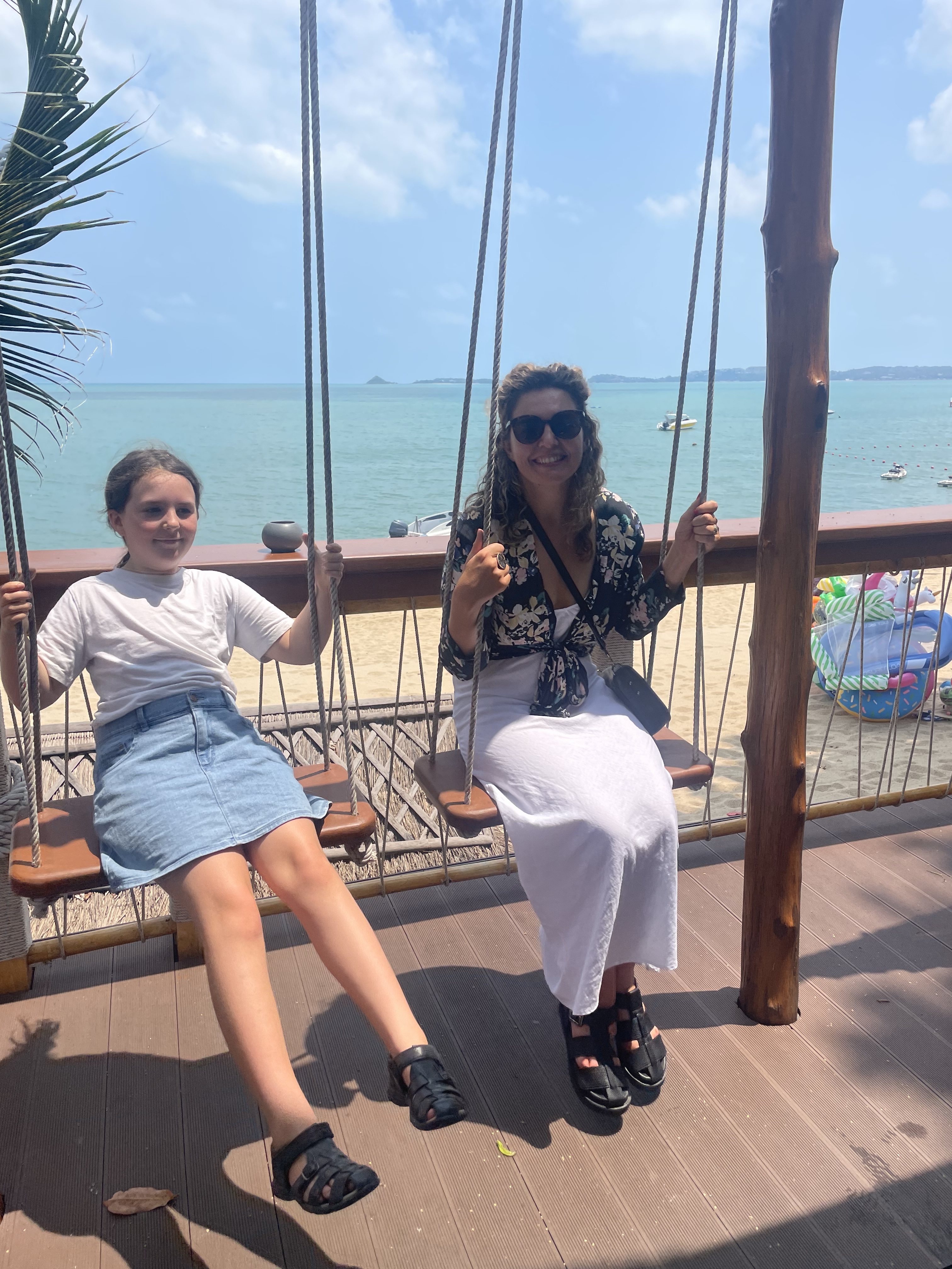 Eliza Hull sitting on a swing at a beach with her child sitting on the swing next to her