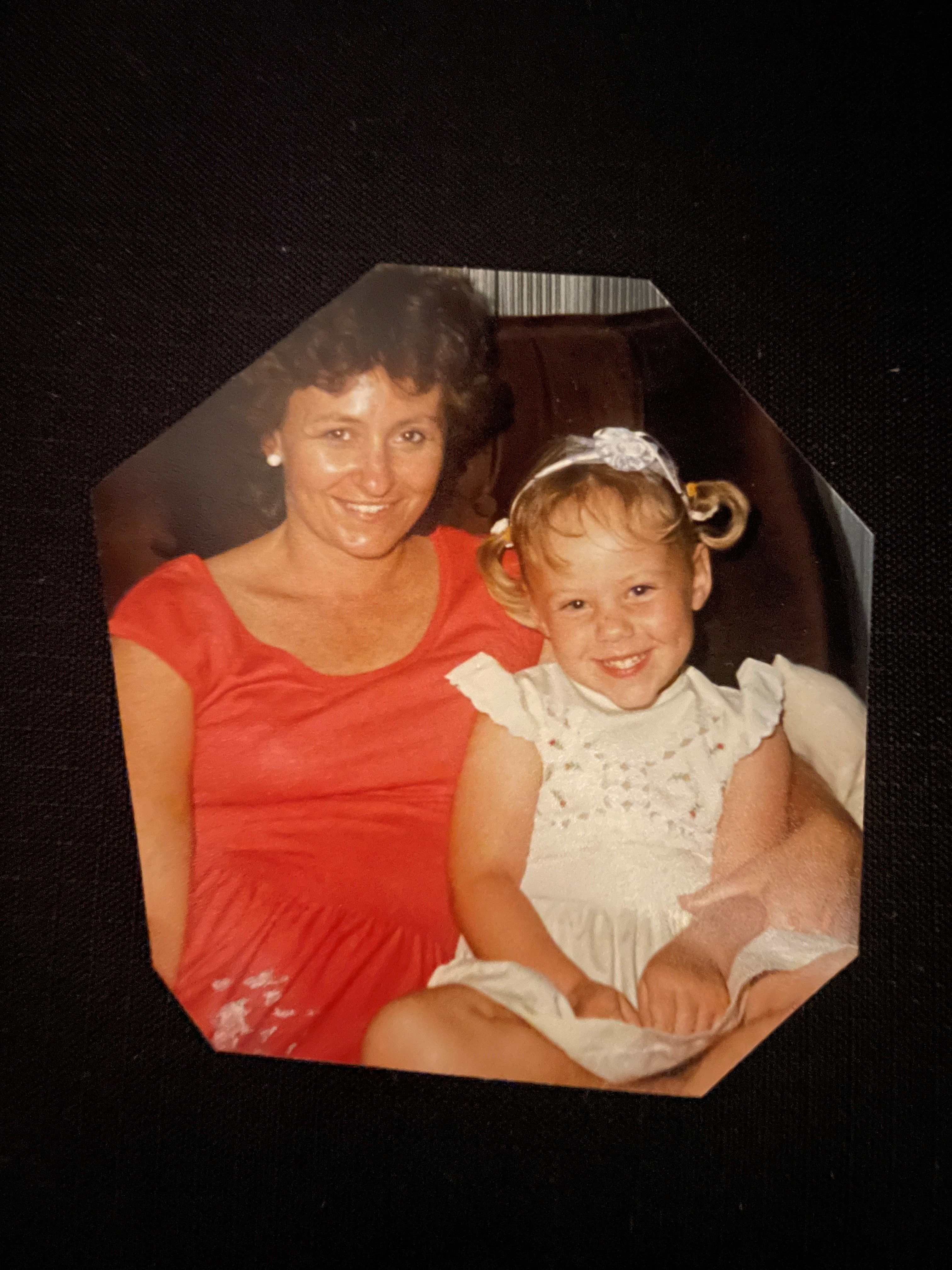 A mother and daughter sitting together on a couch smiling. 