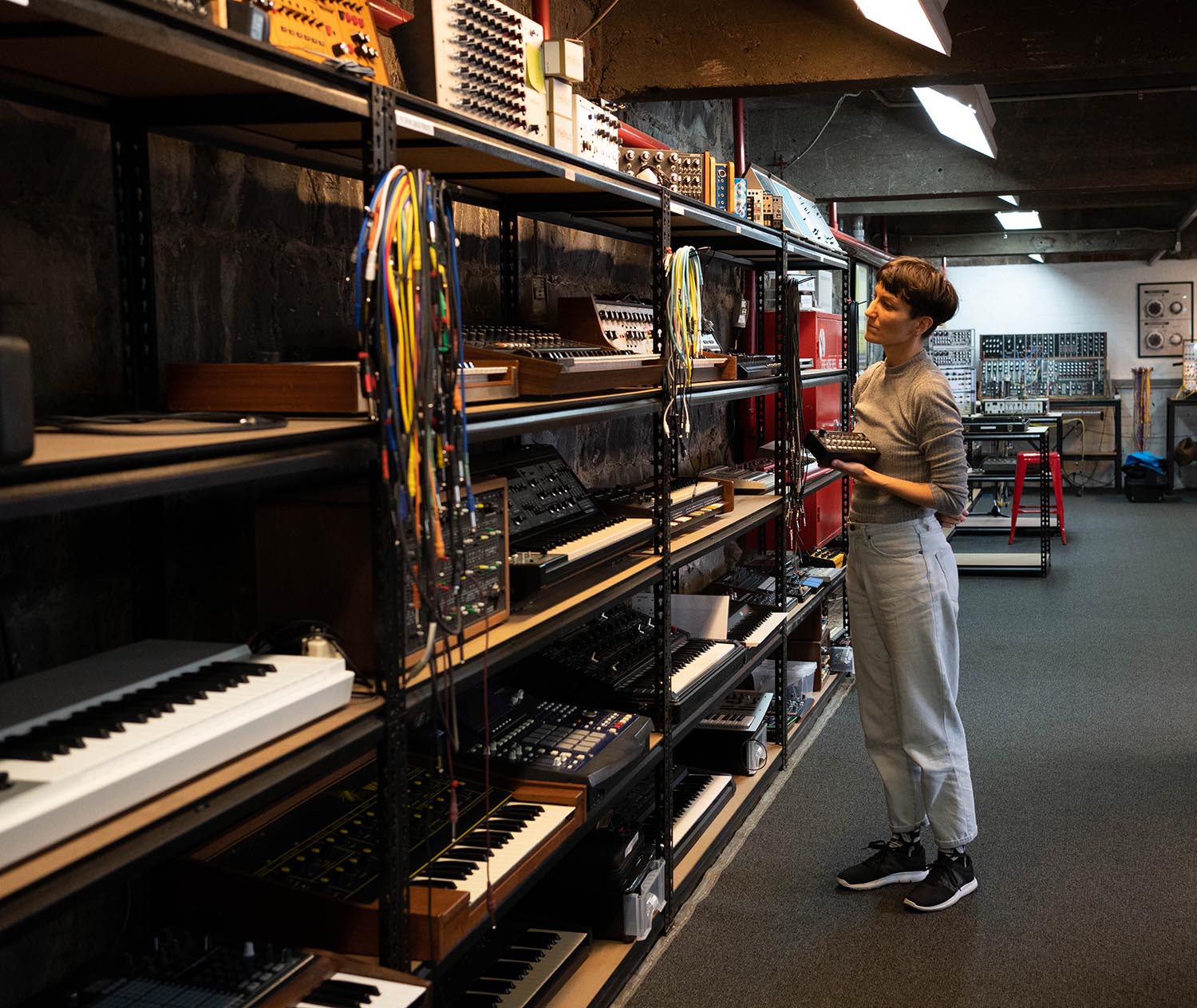 A person in front of shelves holding synthesisers
