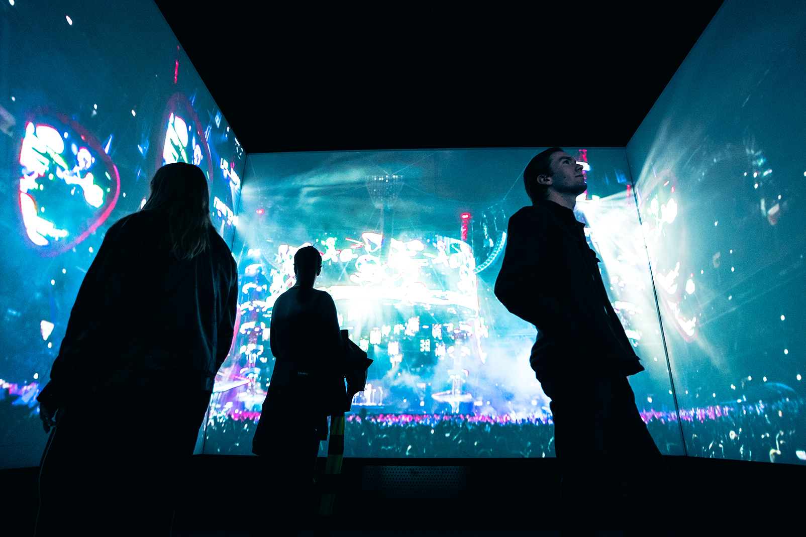 Three people inside the AMV Amplifier - A room lined with large projections playing scenes from a concert.