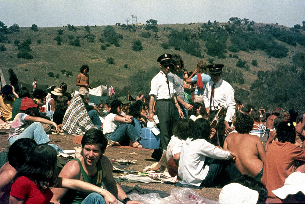 A vintage colour photo of St John's Ambulance officers picking their way through a crowd who are seated on the grass at the Sunbury Music Festival.