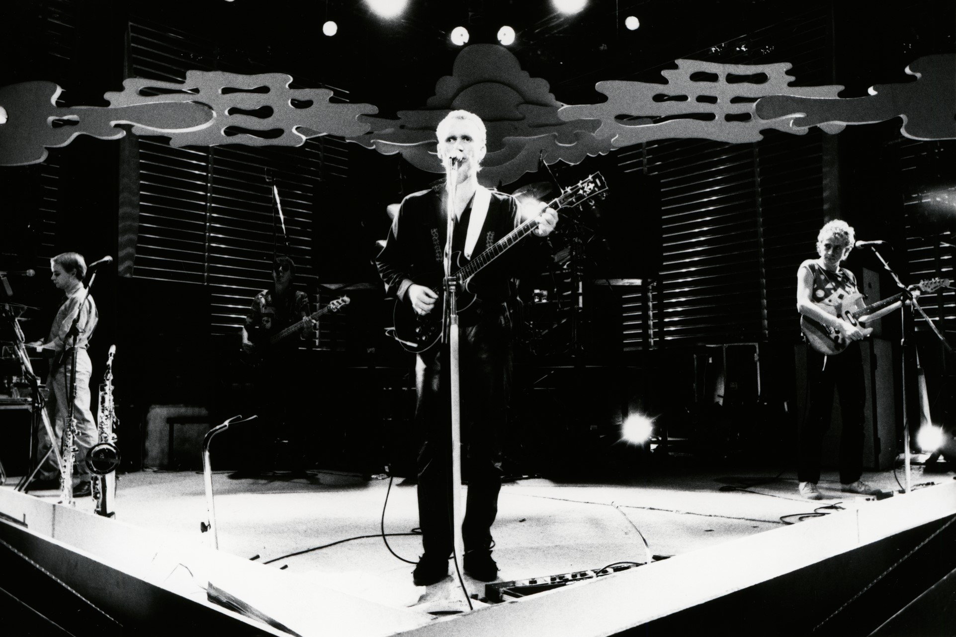 A black and white image of Men at Work performing on stage. 