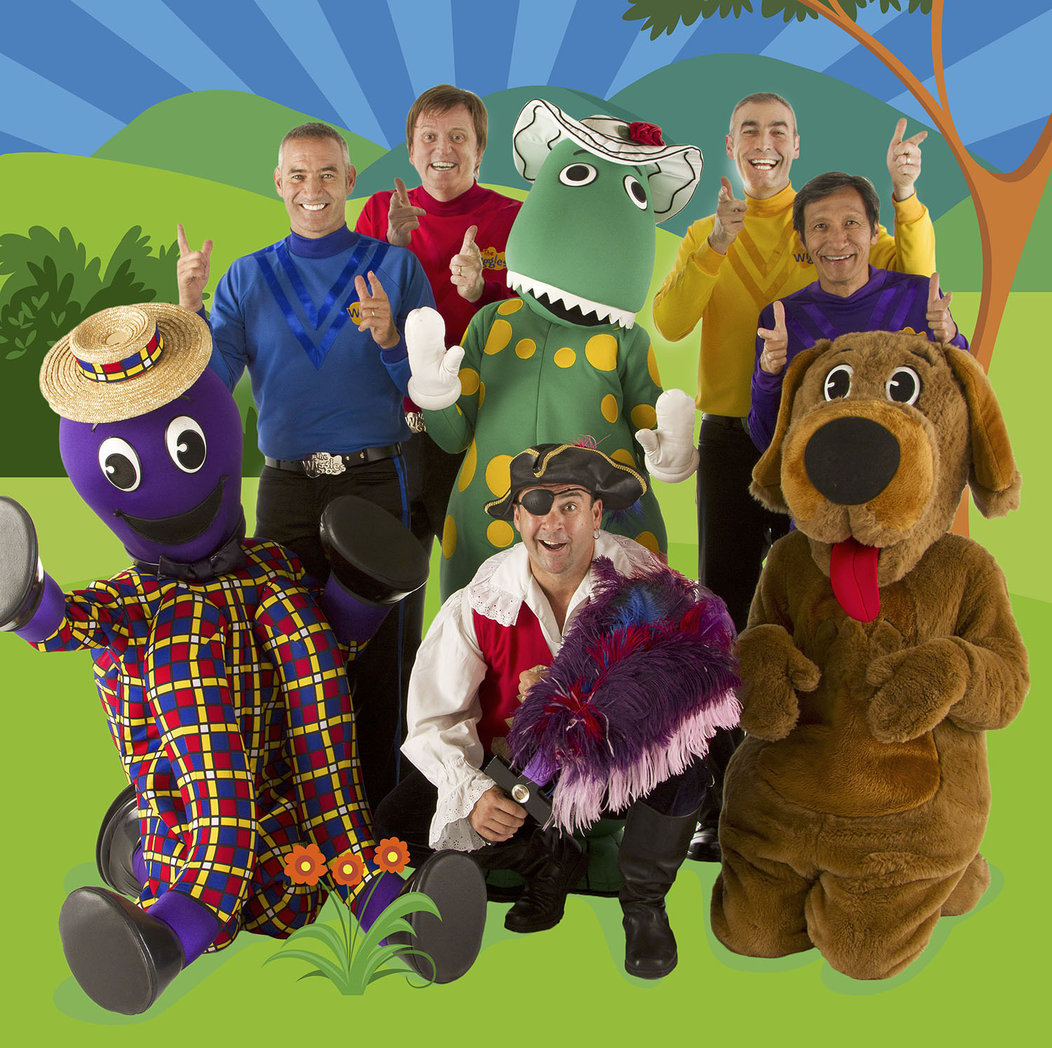 A promotional photo of The Wiggles with Henry the Octopus, Dorothy the Dinosaur, Captain Feathersword and Wags the Dog. The Wiggles are the original four - blue, red, yellow and purple - are they're all smiling and doing finger-guns. Behind them all is a digitally illustrated backdrop showing green grass, bushes, a tree, mountains and a blue sky with radiating dark and light blue lines.