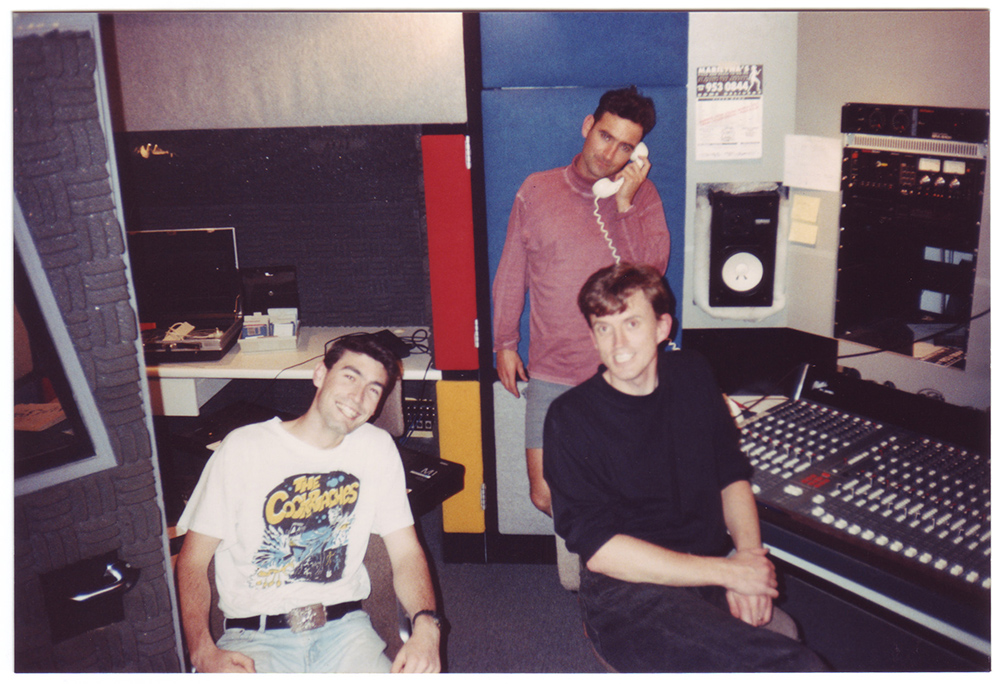 Greg Page, Anthony Field and Murray Cook in a recording studio. Two are sitting in chairs in the foreground, and one is talking on the phone in the background.